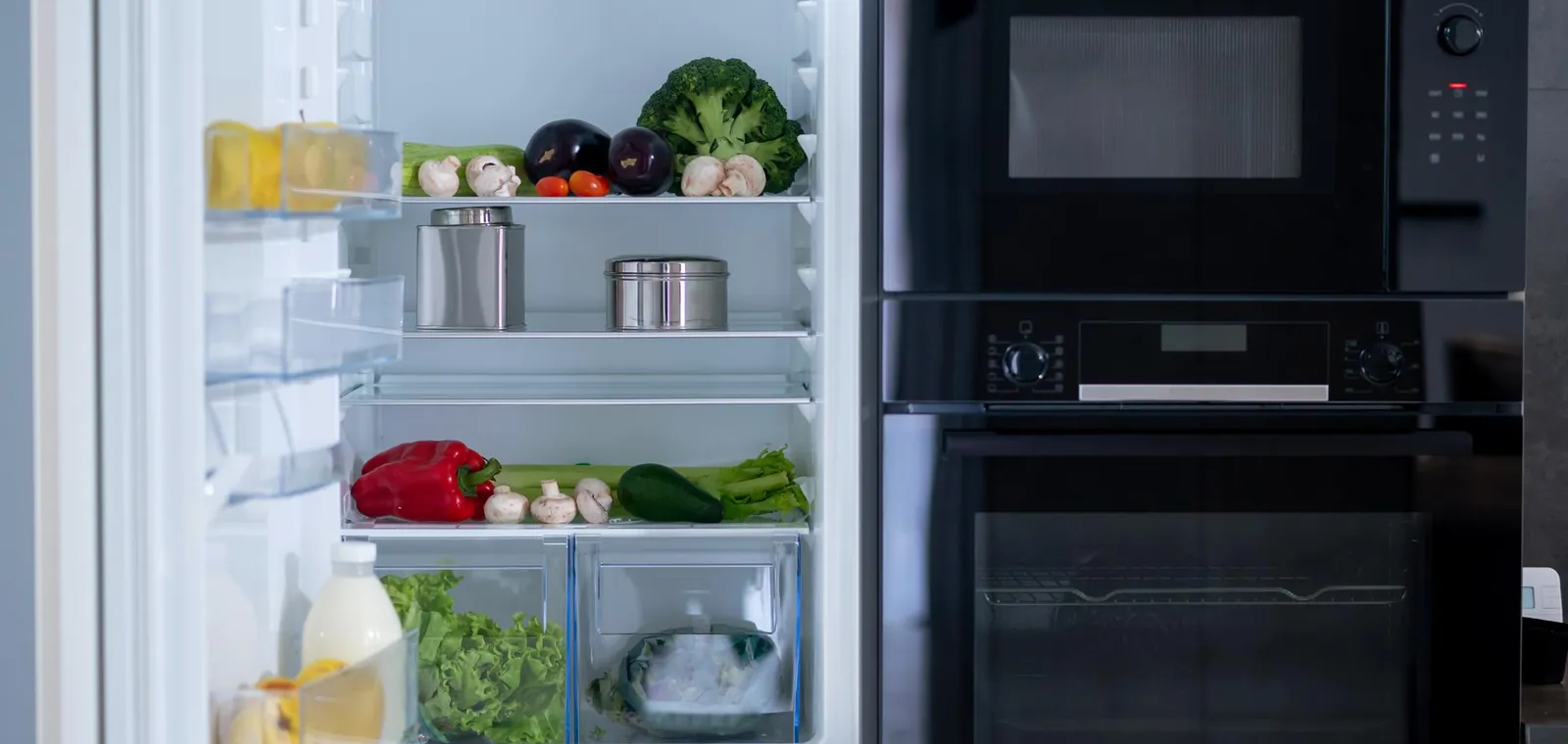 Open refrigerator stocked with fresh food beside a built-in oven